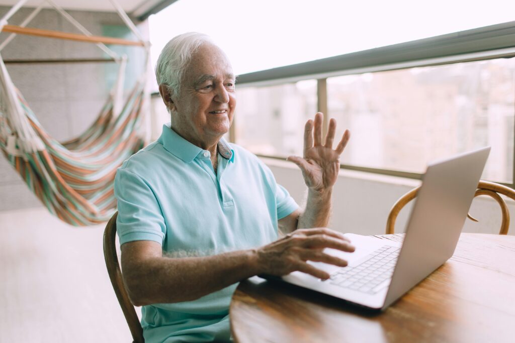 Cette photo montre un homme âgé faisant signe de la main à l'ordinateur devant. Elle démontre que les sites internet doivent être accessibles pour tout type de public (dont les personnes âgées).