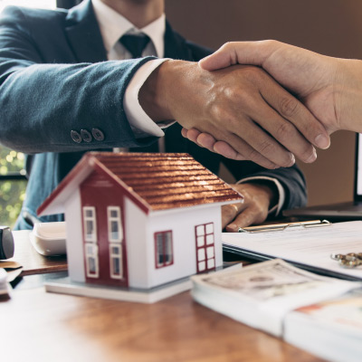 Agents immobiliers se serrant la main au-dessus d'une table avec une maquette de maison, symbolisant un accord réussi