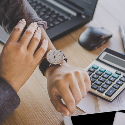 Professionnel vérifiant l'heure sur sa montre tout en travaillant sur des documents financiers avec un calculateur