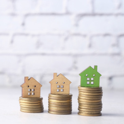 Trois maisons en bois posées sur des piles de pièces de monnaie croissantes, symbolisant l'investissement croissant dans l'immobilier durable