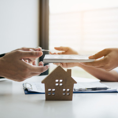 Deux professionnels échangeant des documents avec une maquette de maison en premier plan, illustrant une transaction immobilière réussie
