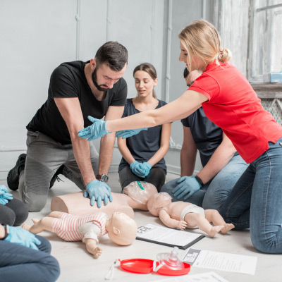 Formation pratique en cours avec un instructeur et des participants pratiquant les gestes de premiers secours sur un mannequin de réanimation